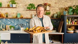 Jamie Oliver holding a chopping board filled with crispy chicken legs for Jamie's 5 Ingredient Meals