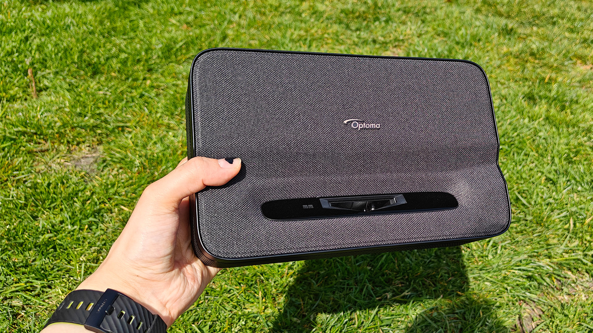 Optoma Photon Go portable UST projector held in hand above grassy lawn