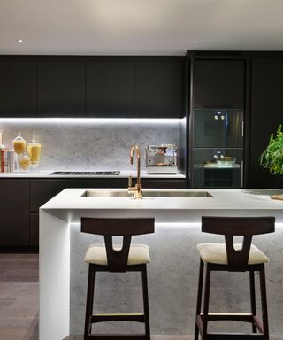A kitchen with black cabinets and a white island with under-counter lighting