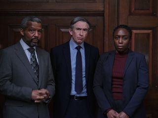 Hugh Quarshie in 'Stepehn' playing Neville Lawrence, Steve Coogan as DCI Clive Driscoll and Sharlene Whyte as Doreen Lawrence, all in suits and standing in a dark panelled room