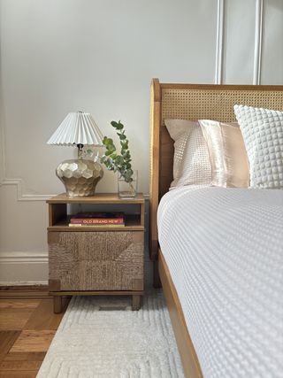 a bed with a rattan bed-frame a natural woven-detail nightstand with a gold-detailed lamp base and fresh eucalyptus in a glass