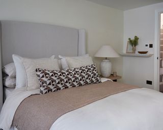 neutral bedroom with oversized winged headboard and patterned long cushion