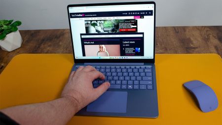 A masculine hand typing on a Microsoft Surface Laptop 13-inch