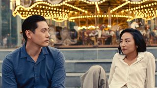 Teo Yoo and Greta Lee as Hae Sung and Na Young in front of a carousel in Past Lives