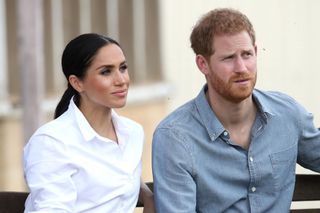 Meghan Markle in a white shirt sat next to Prince Harry in a blue shirt looking on with inquisitive faces.