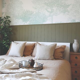 A bedroom with half-height tongue-and-groove wall panelling in sage green with the top half of the wall covered in a tree-print mural