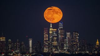 orange hued full moon rises above the New York skyline.