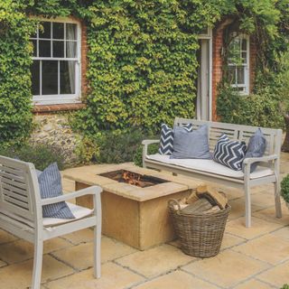 Cottage patio garden with bench seating around a stone fire pit, and greenery growing on the outside of the house