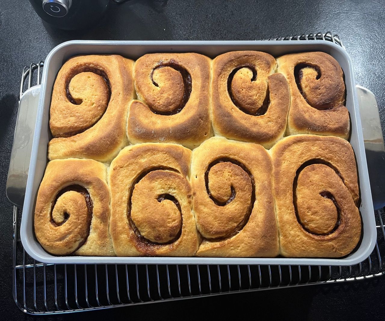 Golden risen cinnamon rolls inside a rectangular baking tin