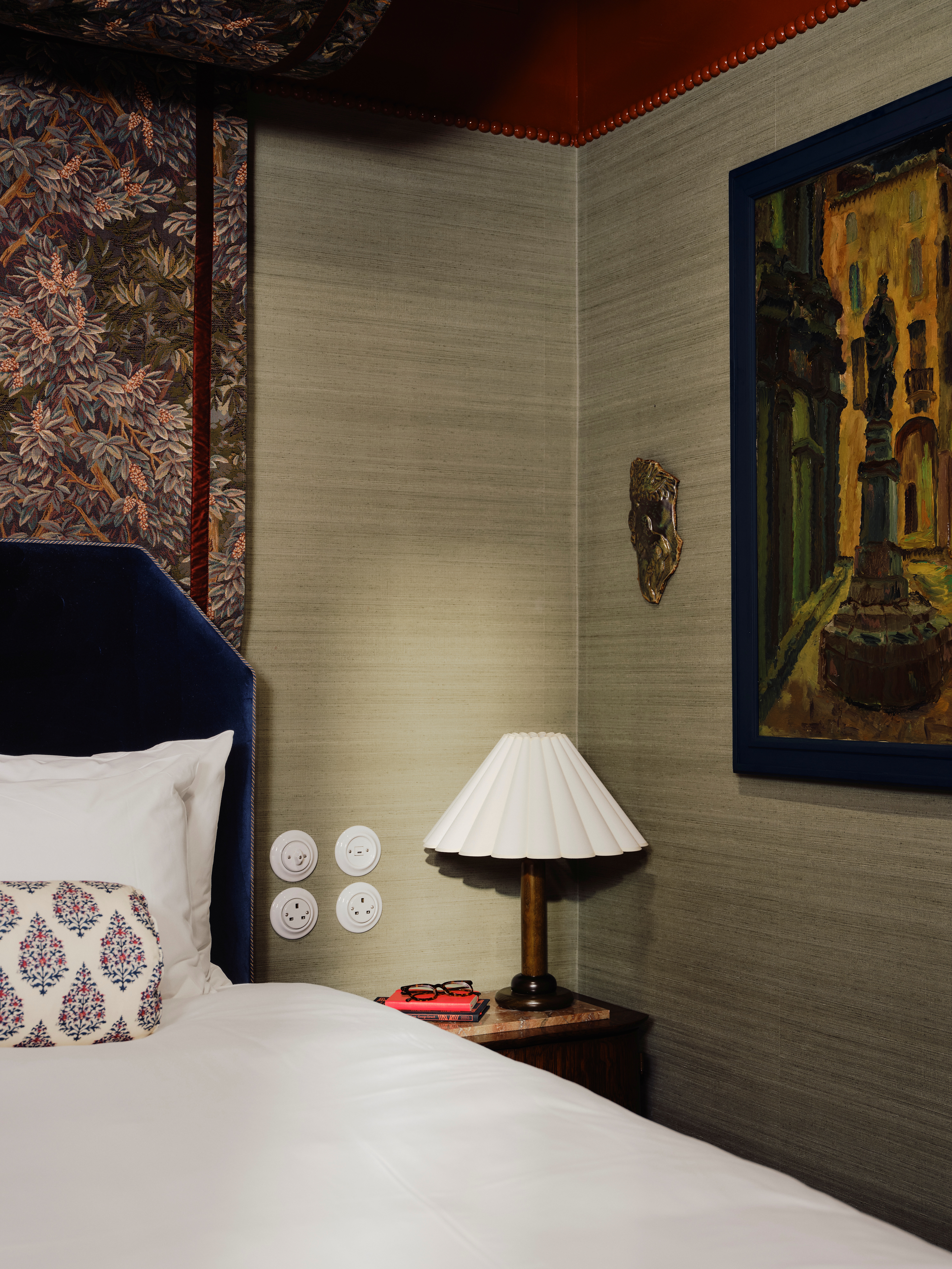 A maximalist hotel room wrapped in patterned tapestries, eclectic framed artworks, velvety surfaces, colorful tiles, and contrasting motifs spanning the hues of green, blue, red, cream, and bordeaux.