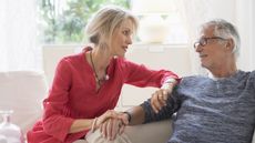 A senior couple sit on a couch talking.