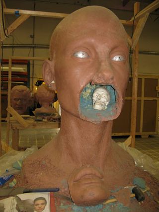 A huge sculpture that looks like a bald woman with a skull in the mouth made out of clay.