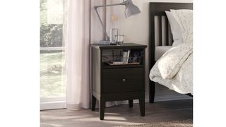 IKEA Idanäs Nightstand in Brown in a bedroom with a lamp and water on top, next to a window with white curtains, and a black bedframe