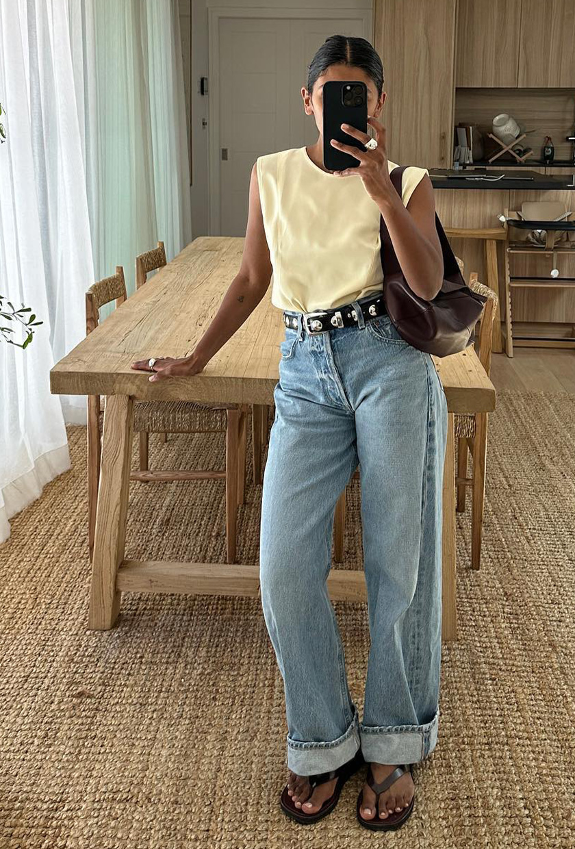 A woman wearing a satin tank top, light-wash jeans, and flip-flops.