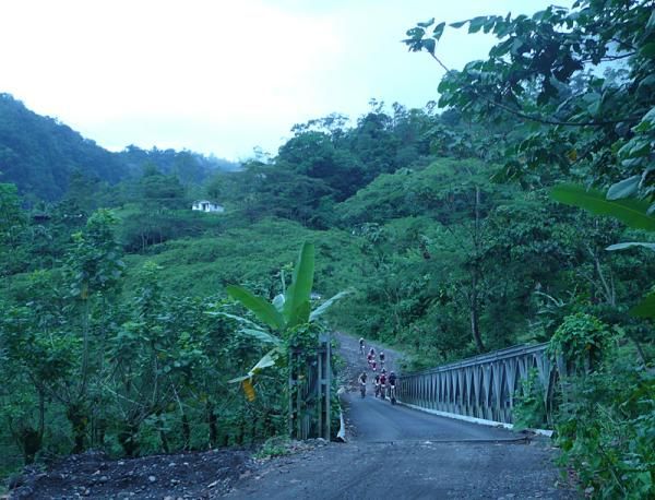 The men's lead group crosses a bridge after a high speed downhill.