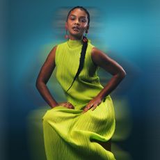 Celeste O'Connor posing in a sleeveless chartreuse dress with mock neck. 
