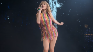 Taylor Swift in a rainbow dress singing during the Reputation Stadium Tour.
