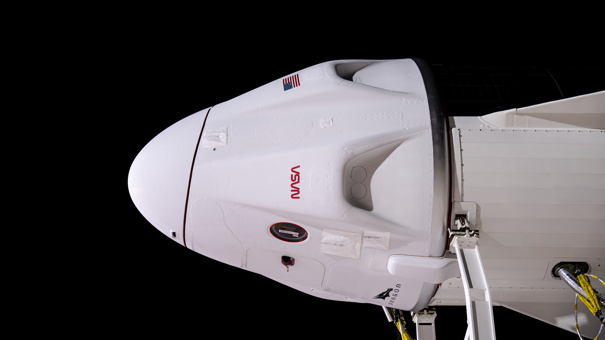 a white spacex dragon capsule is seen horizontally, pointing to the left, against a black background.