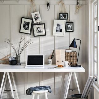 room with laptop white table hanging frames and table lamp