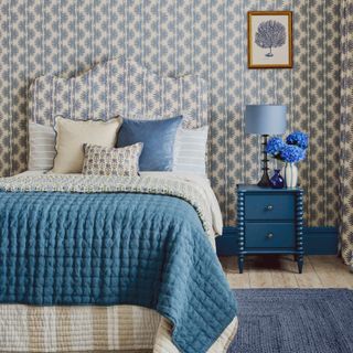 A bedroom with a patterned wallpaper matching the scalloped bed hadboard