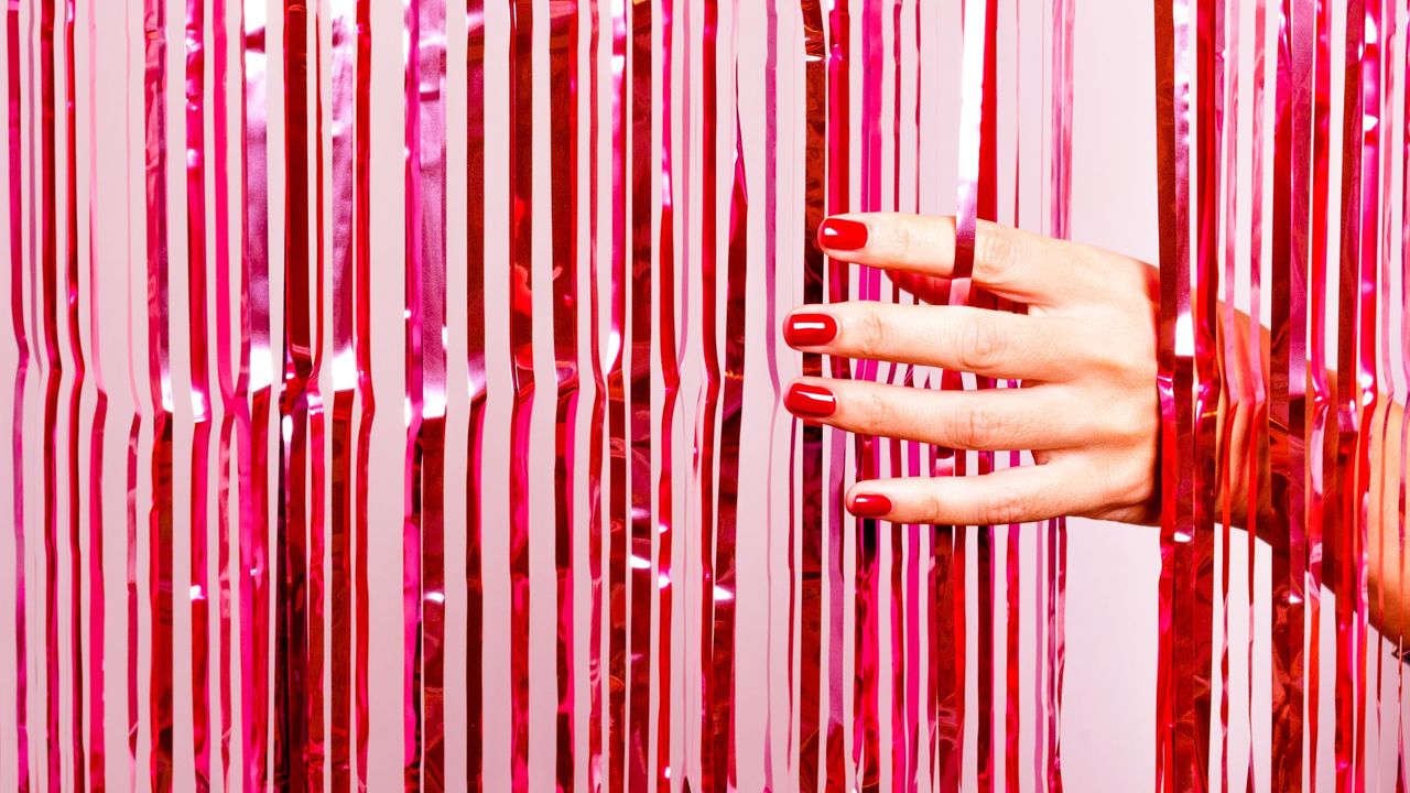 Hand with red nails moving through pink tinsel curtain