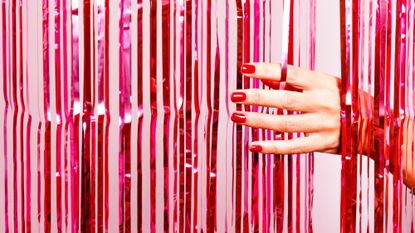 Hand with red nails moving through tinsel curtain
