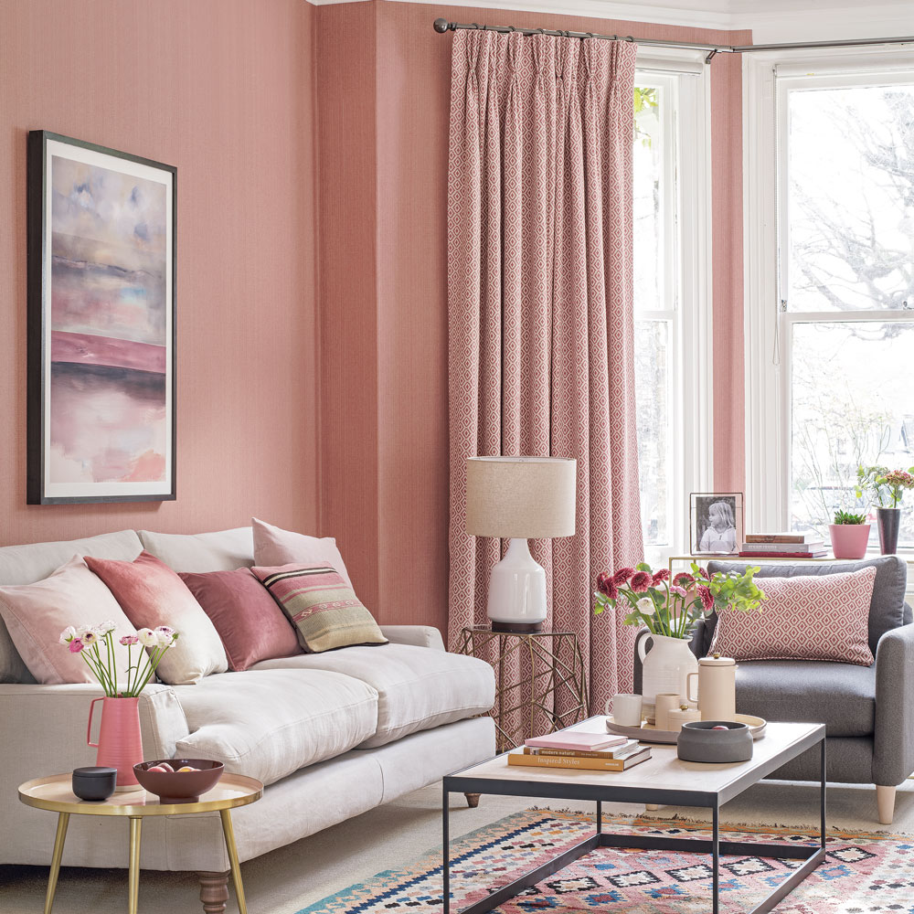 pink living room with pink walls and curtains, white and grey sofas with pink cushions, a colourful pink pattern rug and an industrial style coffee table on top