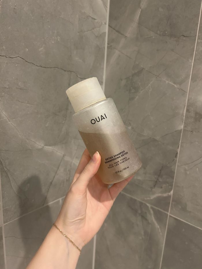 A picture of junior beauty editor, Grace Lindsay, holding the Ouai detox shampoo in a marble bathroom