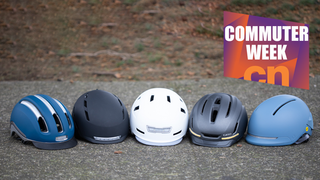 Five ebike helmets all sitting on the ground. Image is overlaid with a commuter-week badge