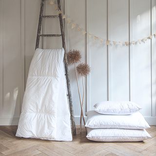 A duvet hung on a ladder with a stack of three pillows next to it