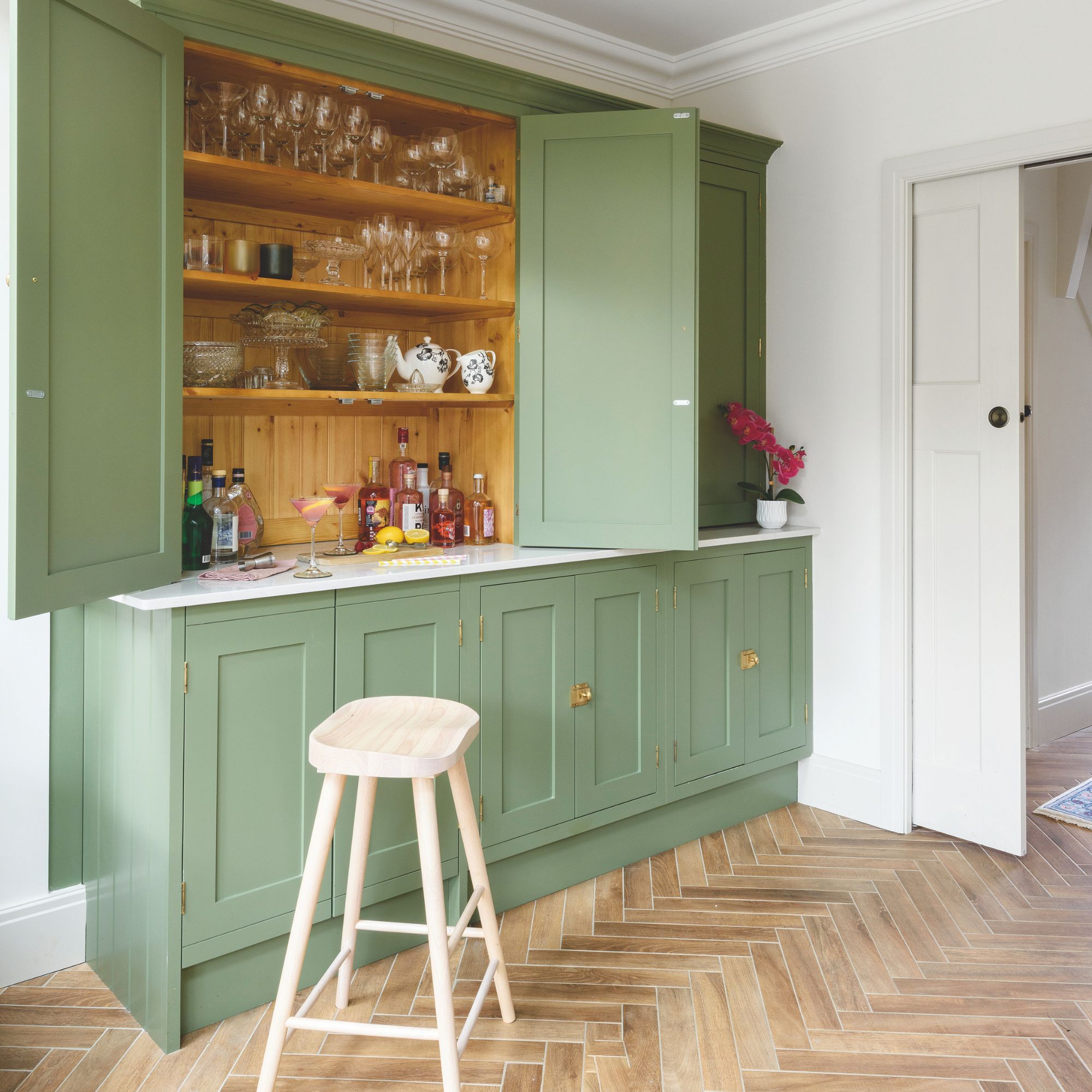 Kitchen with wooden herringbone flooring and grey kitchen cabinets opened up to create a bar area