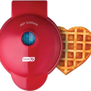A product image of a mini red waffle maker with a heart shaped waffle next to it