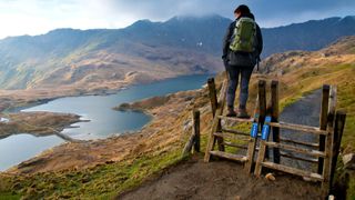 A woman hiker standing on a stile on the Pyg track towards the summit of Snowdon, Wales