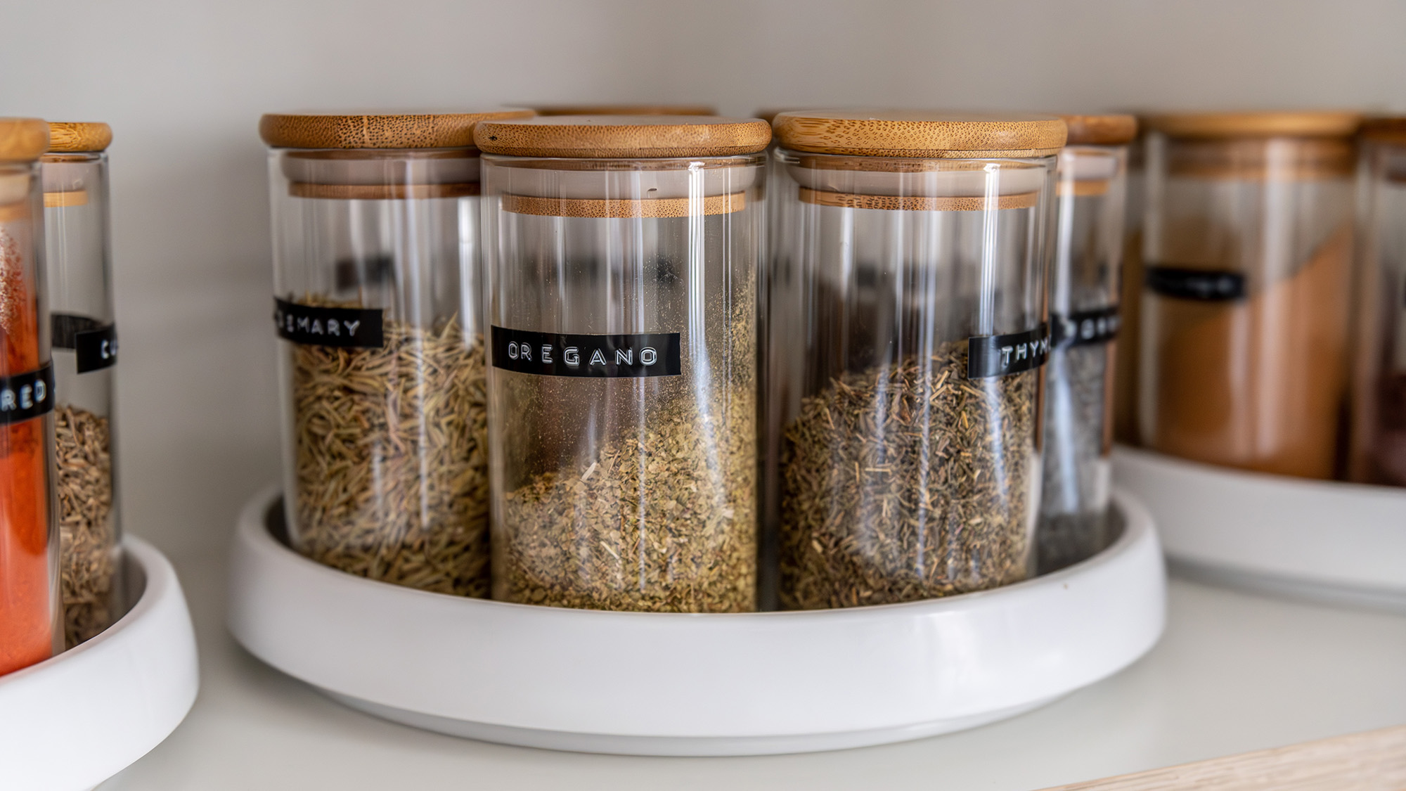 Neatly organized labeled food pantry in a home kitchen with spices in glass wooden spice jars