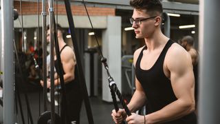 Man using cable machine to perform triceps pull-down arms exercise