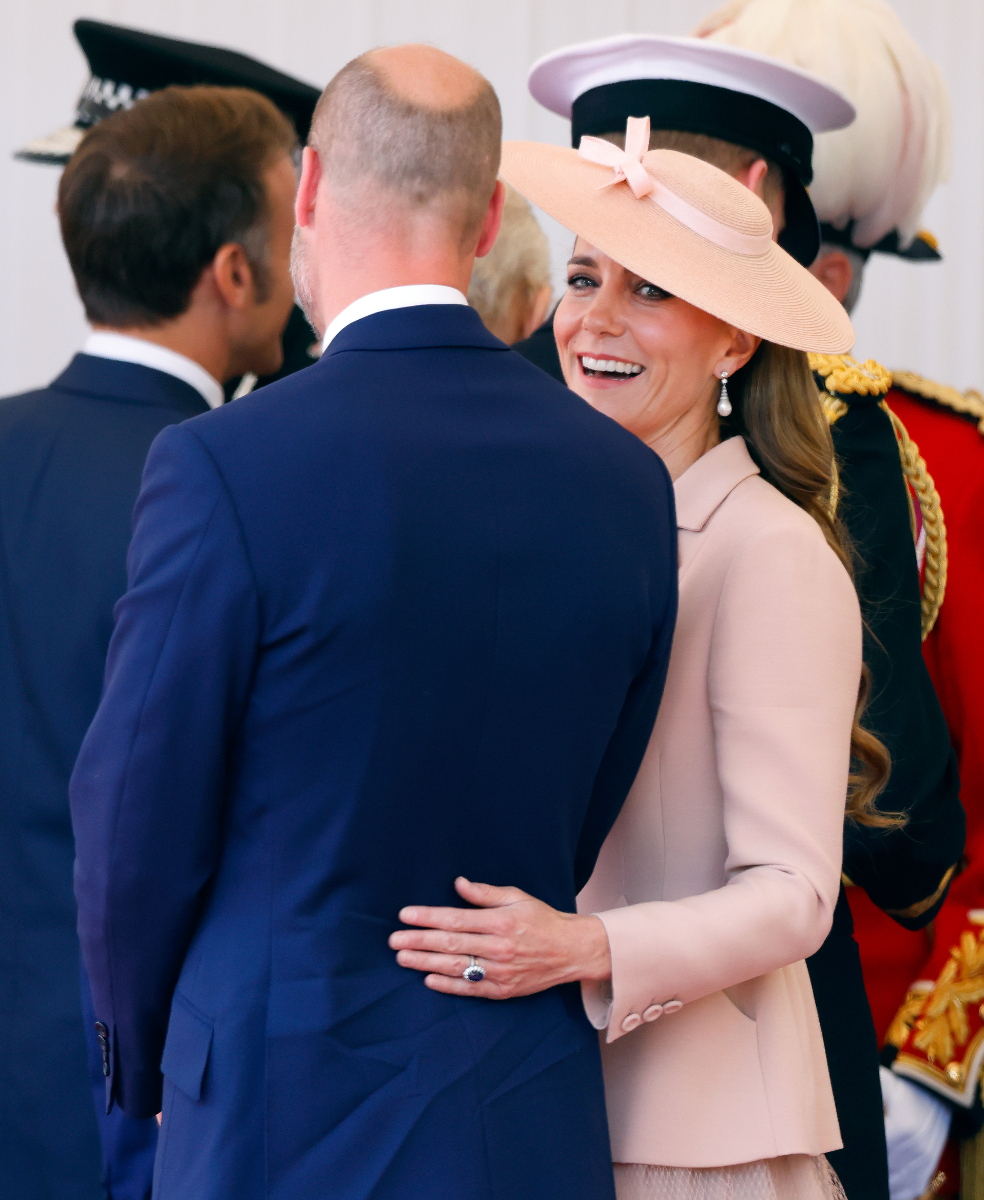 Kate Middleton wearing a pink coat and hat putting her arm around William&#039;s back