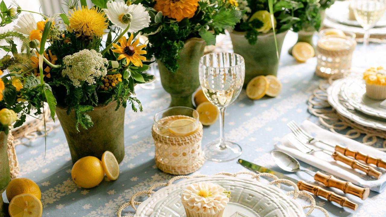 a table setting with potted flowers, bamboo cutlery and lemons