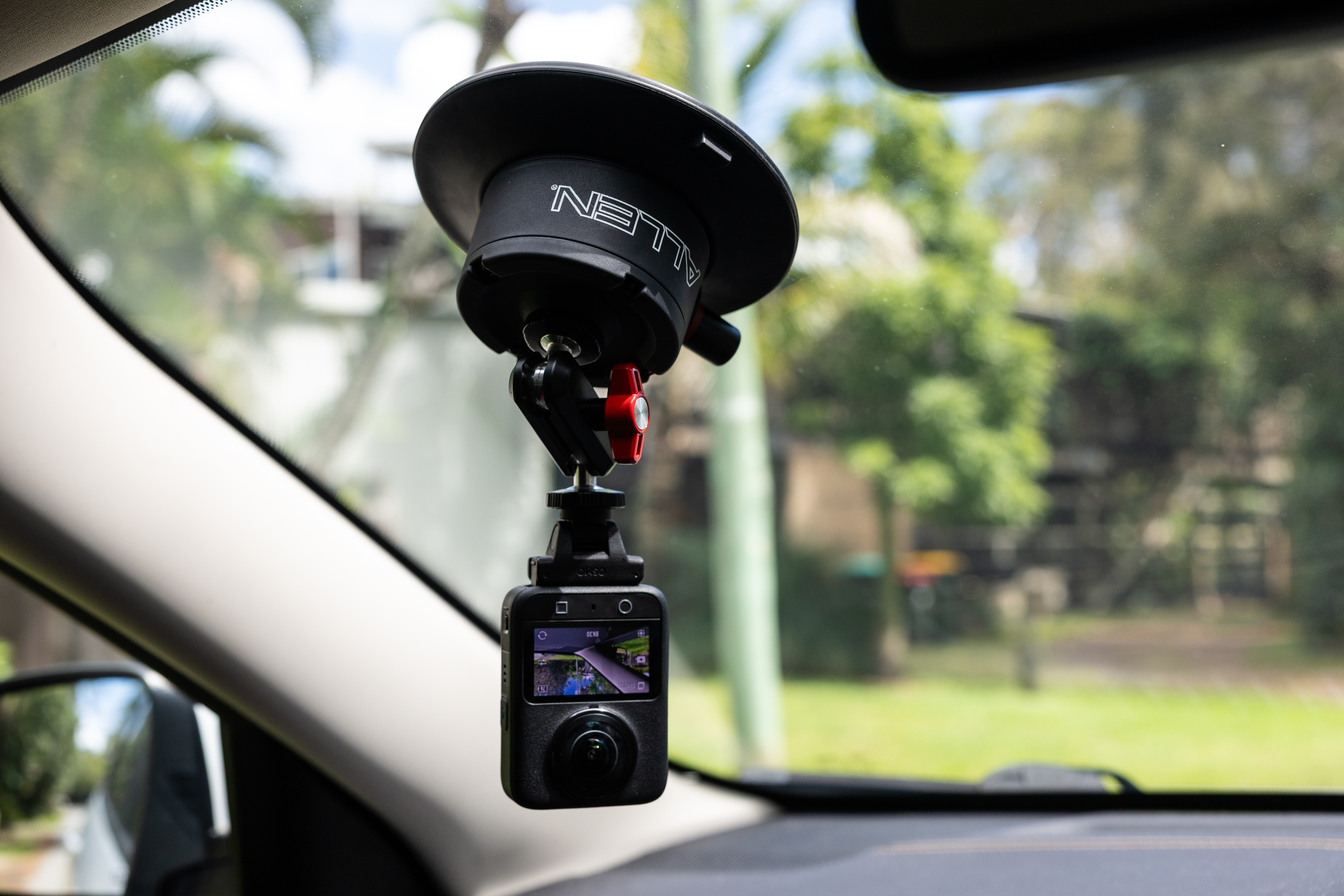 An Allen Smart Suction Snap Camera Mount is attached to the interior of a car windshield, holding a DJI action camera in an underslung position to record the drive.