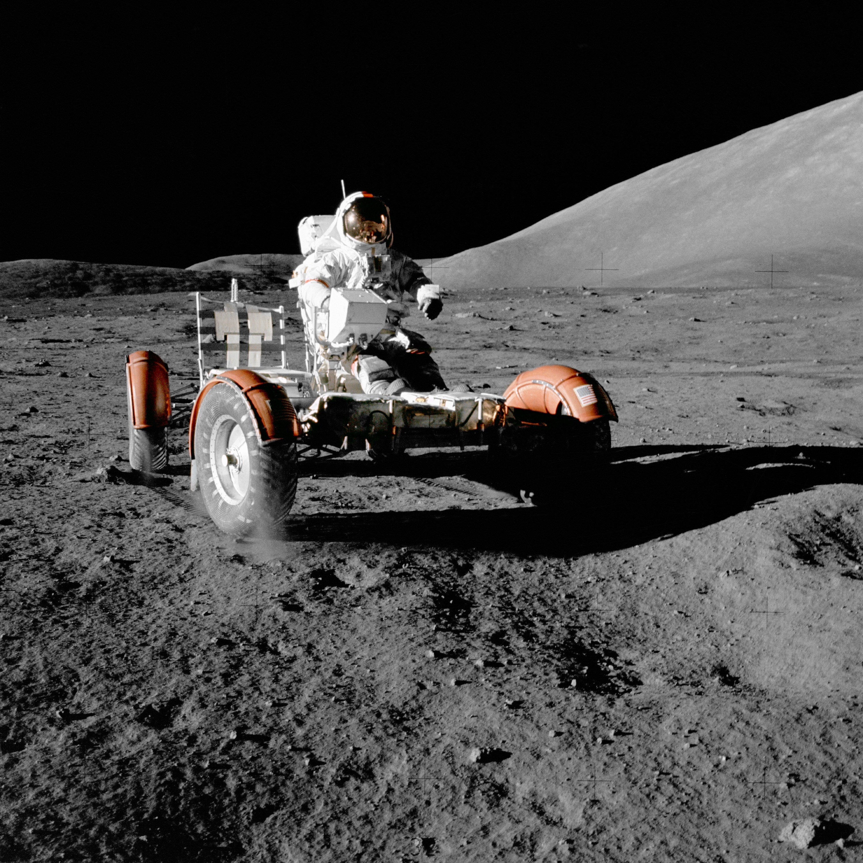 A box with four wheels has a man sitting on it over a grey surface