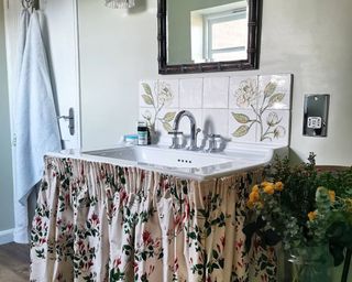 Bathroom sink with cream and green floral curtain around it and plant patterned tiles on the backsplash