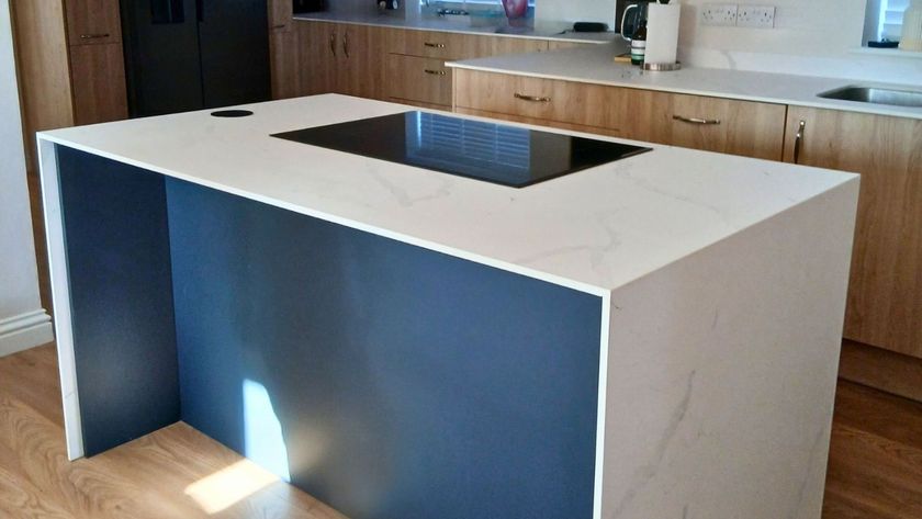 A modern kitchen island with a white marble-effect worktop features subtle grey veining and a sleek black induction hob set flush into the surface.