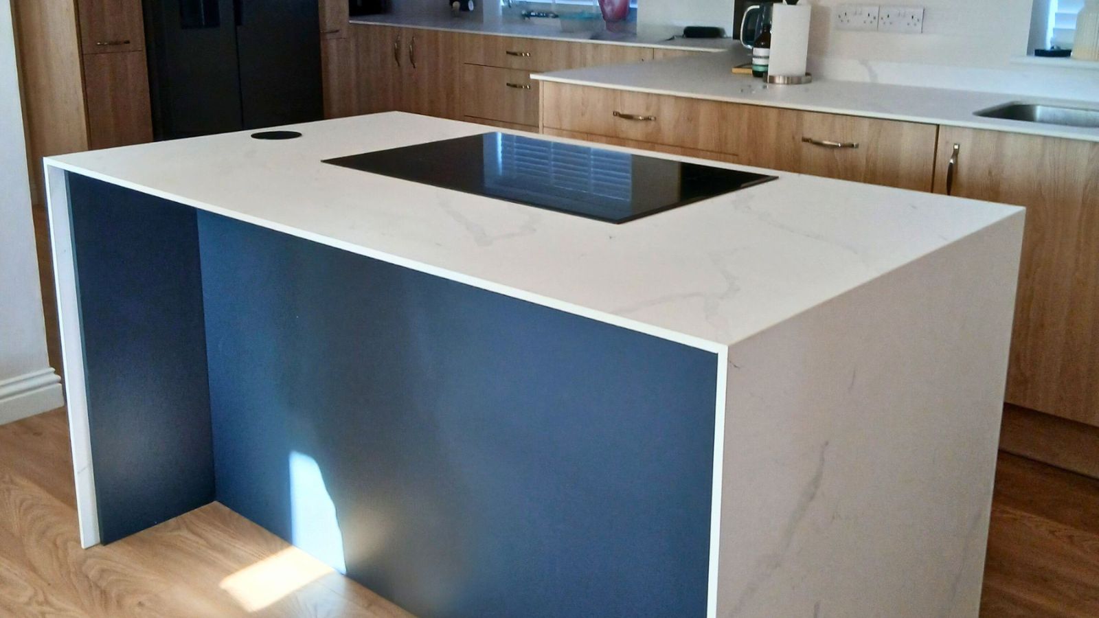 A modern kitchen island with a white marble-effect worktop features subtle grey veining and a sleek black induction hob set flush into the surface.