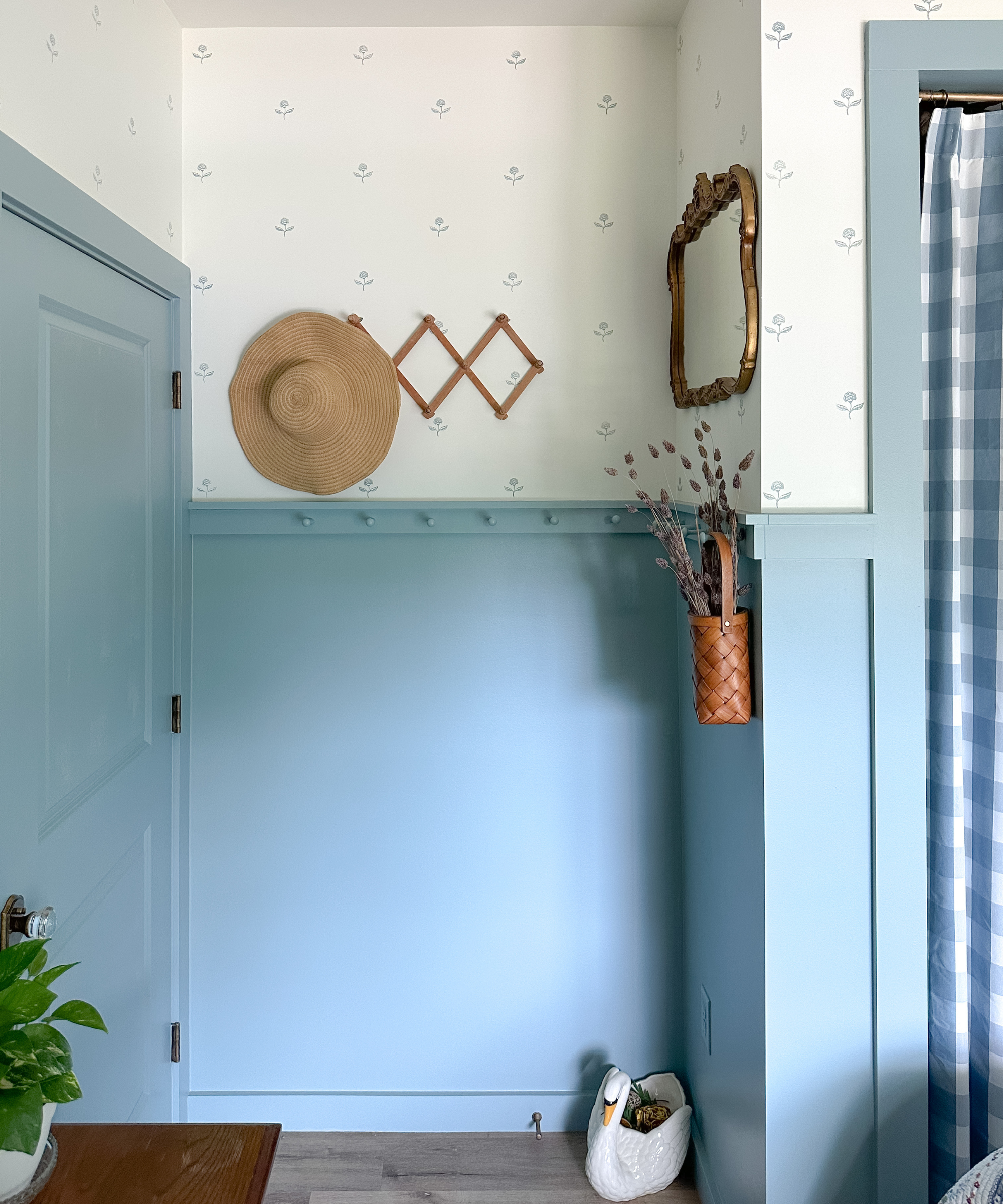 an entrance to a bedroom with a blue painted door, a hook holding a hat, a basket of lavender, and a vintage mirror