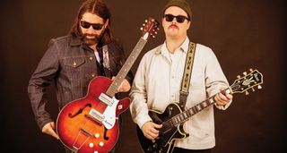 GA-20’s Matt Stubbs and Cody Nilsen wear shades and pose with single-cut guitars against a brown background.