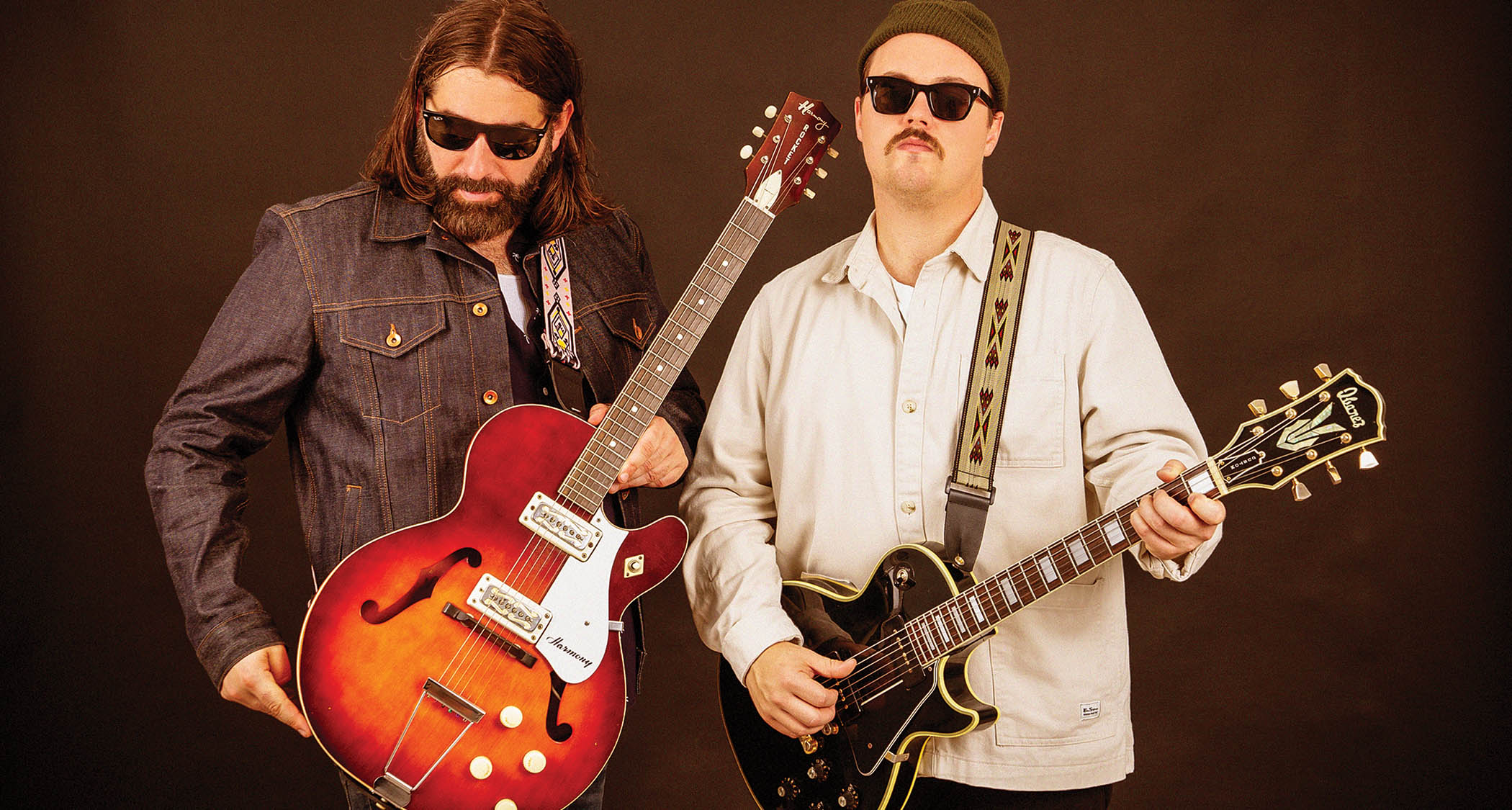 GA-20’s Matt Stubbs and Cody Nilsen wear shades and pose with single-cut guitars against a brown background