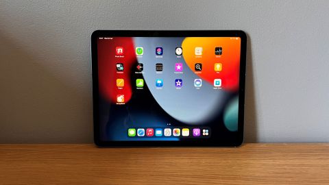 Image shows the iPad Air turned on resting on a wooden table, the screen displaying apps.