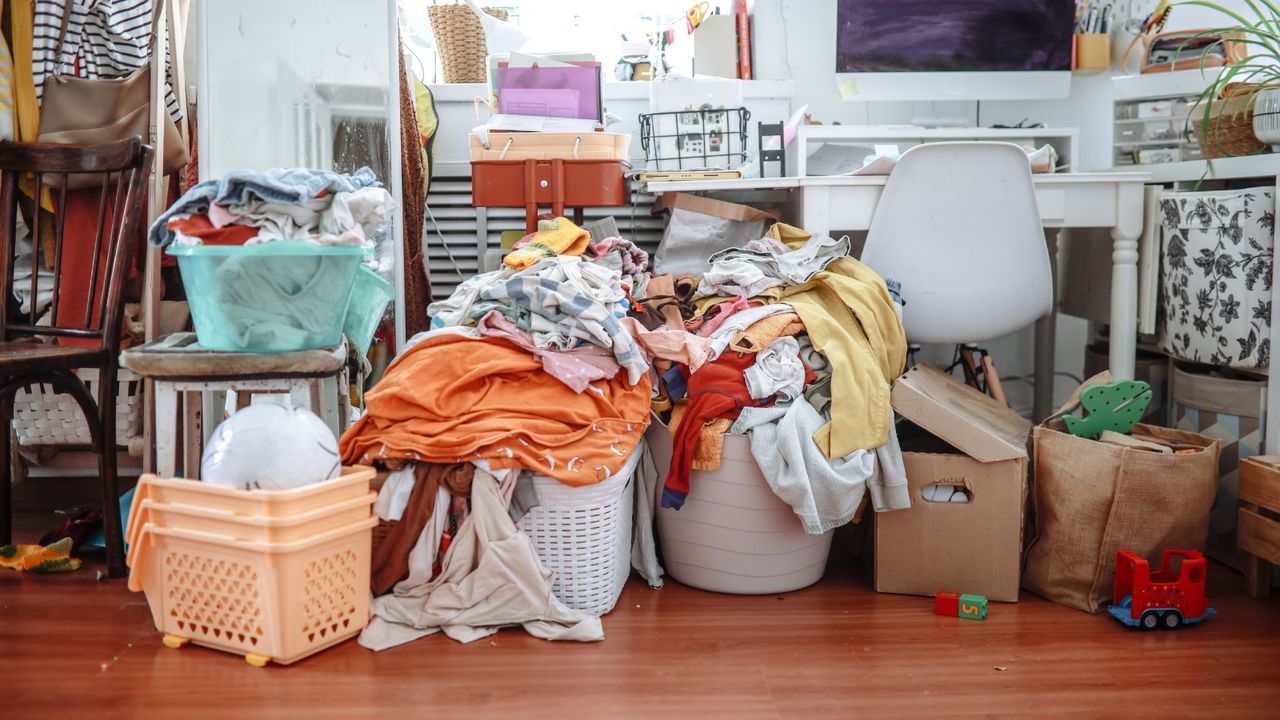 room with baskets of laundry piled up, desk, chair, boxes
