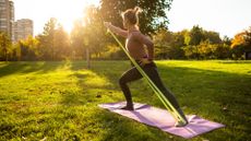 Woman doing 10-minute resistance band workout from yoga mat in sunshine