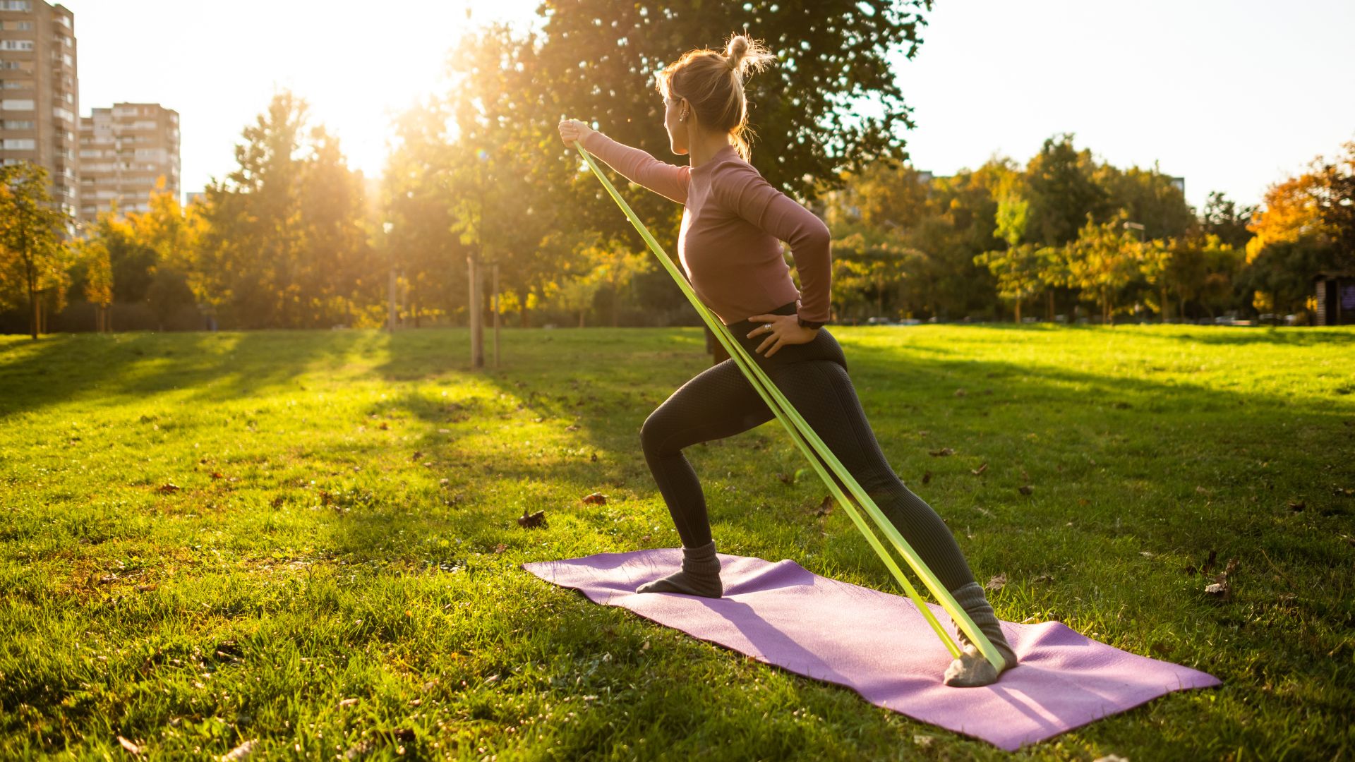 Woman doing 10-minute resistance band workout from yoga mat in sunshine