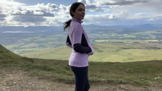 Hiker with hands in pockets wearing a purple fleece looking at the view